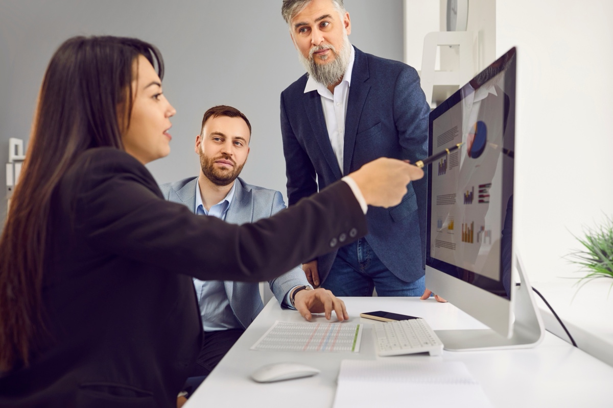Three colleagues reviewing charts and data on a large monitor in an office