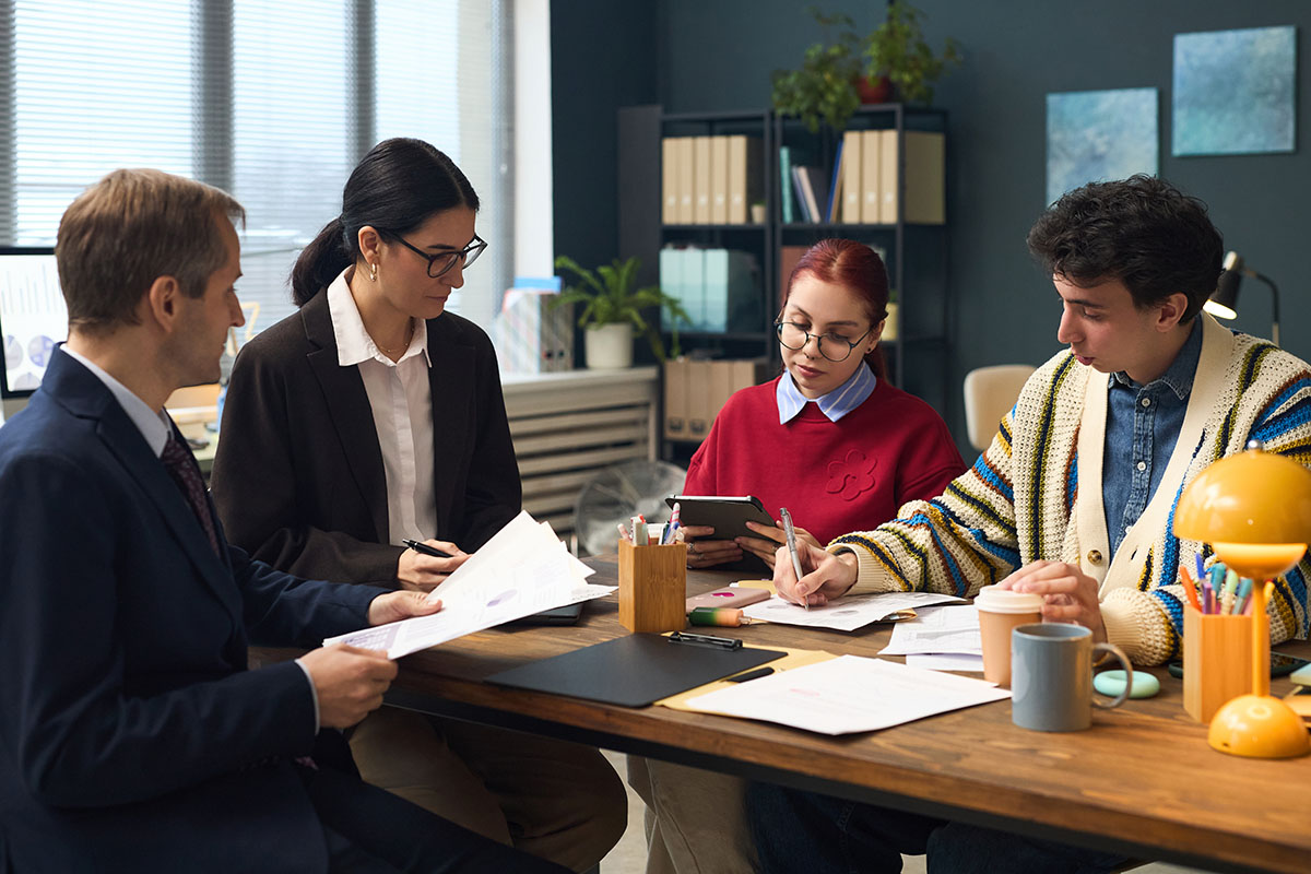 Multiethnic team of colleagues reviewing compliance documents together at an office table