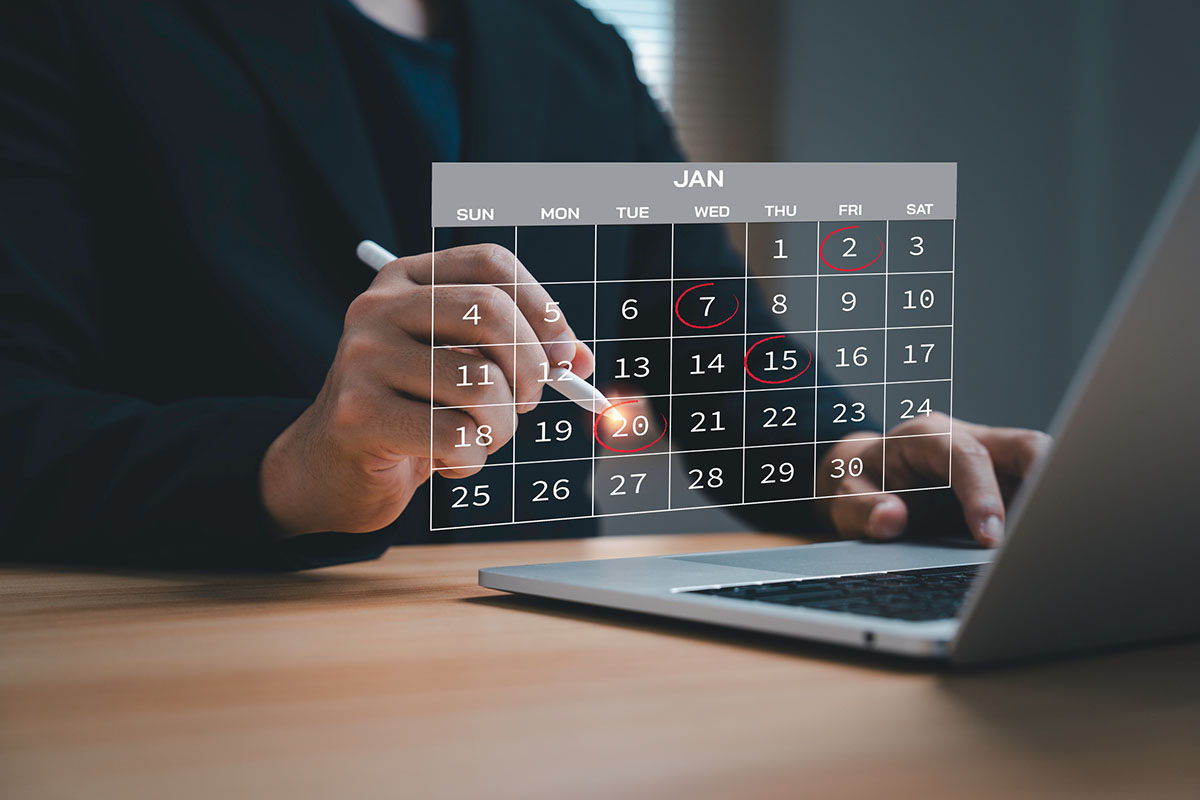 A professional marking dates on a digital calendar overlay above a laptop on a wooden desk