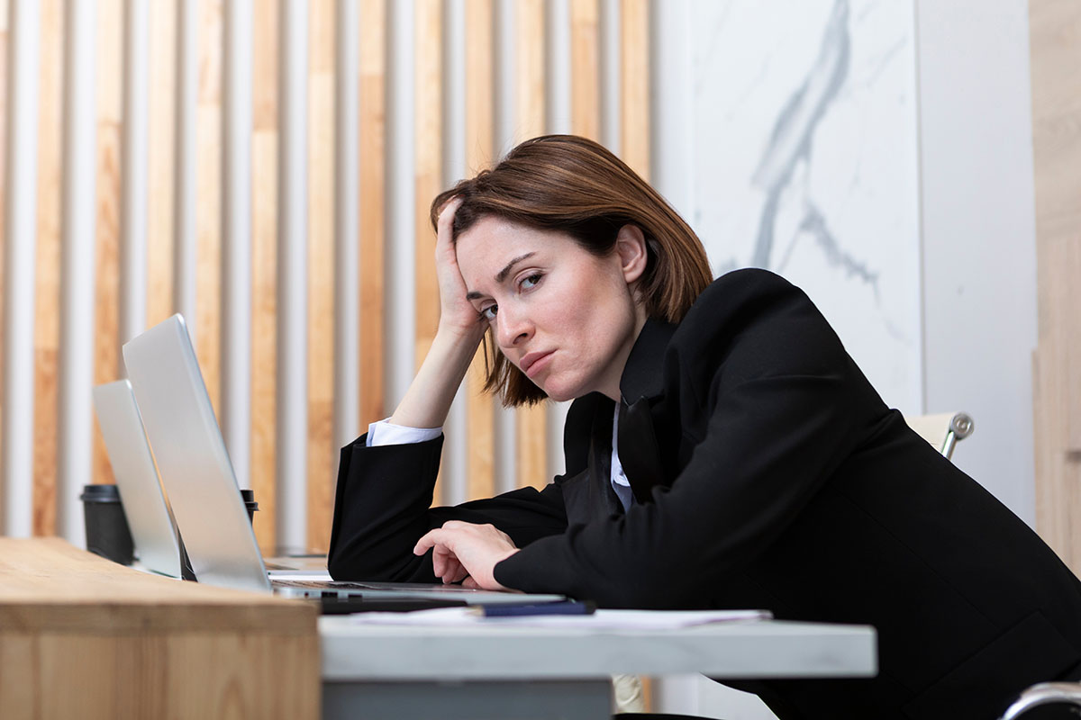 A stressed HR professional resting her head in her hand at her desk, laptop open, surrounded by paperwork