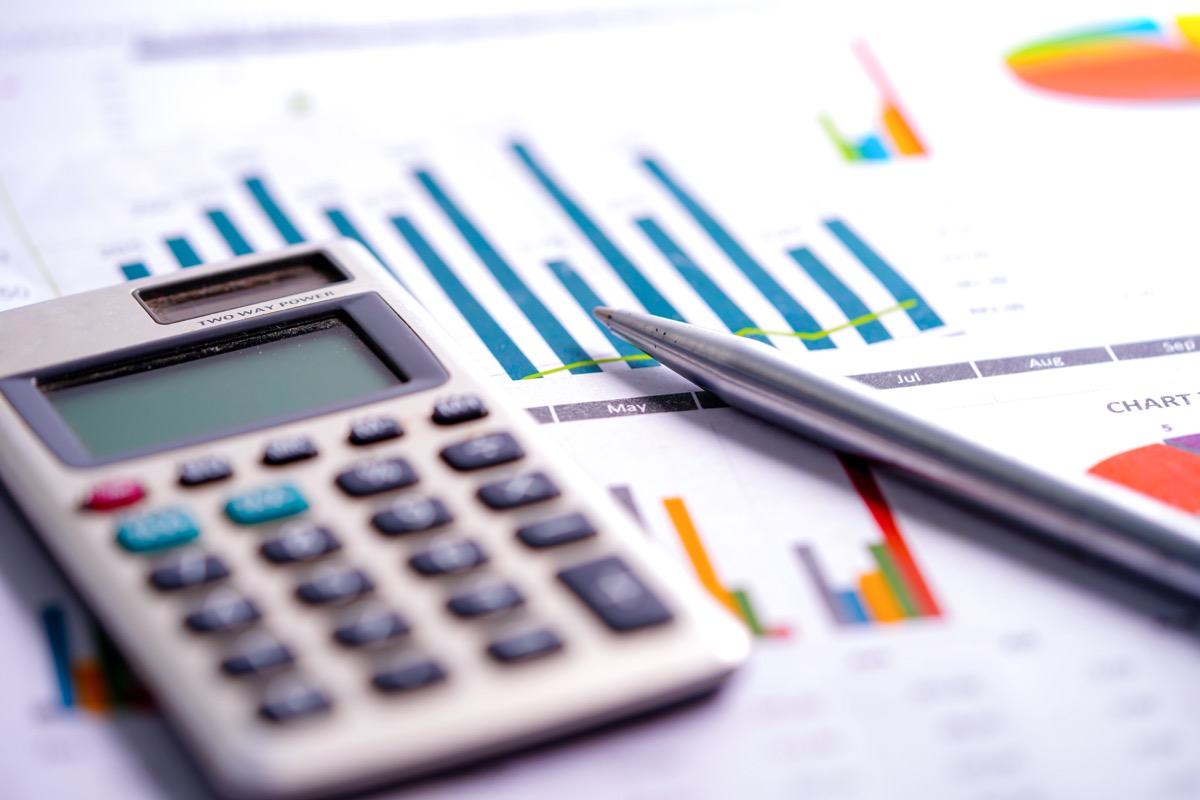 A pocket calculator and a pen resting on printed bar charts and spreadsheets