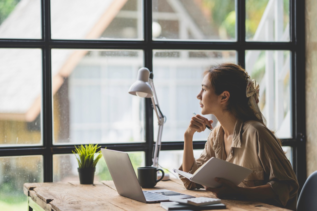 An employee sitting at her desk looking out an office window, thinking