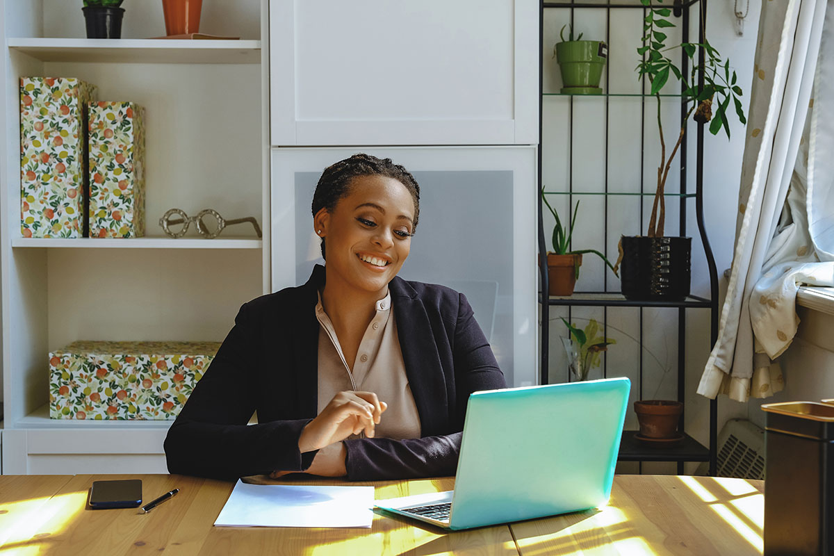A small business owner smiling during a video call on her laptop at a home office desk