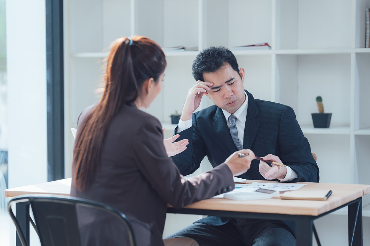 A manager and an employee in business attire in a serious discussion at a desk, reviewing pay documents with expressions of concern