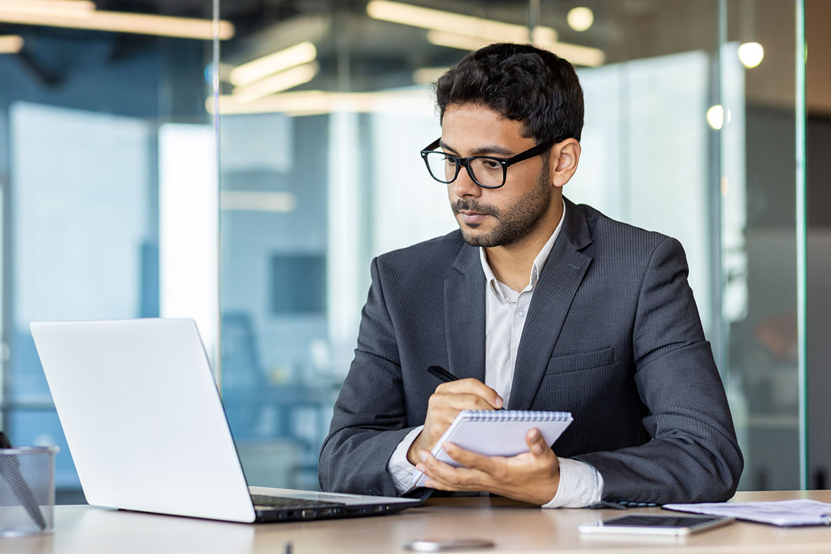 Professional at a desk watching an online course on a laptop while taking notes